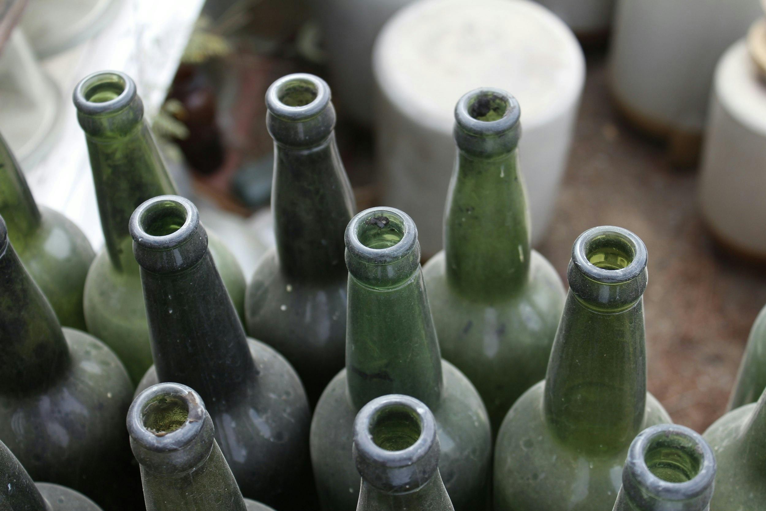 Bottiglie in vetro di colore verde, stappate e sporche di polvere.