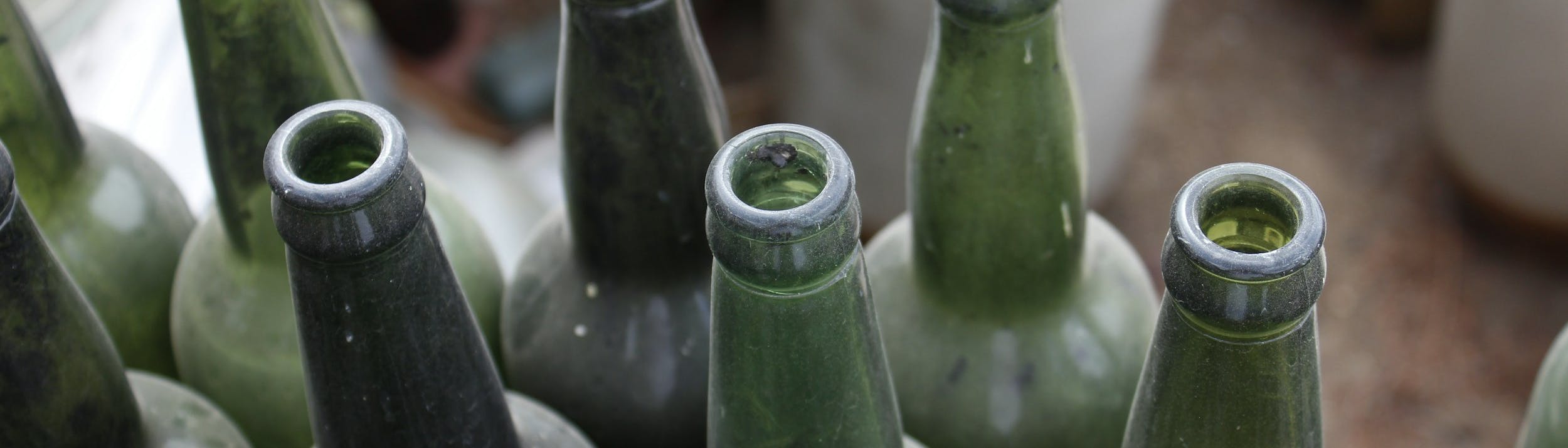 Bottiglie in vetro di colore verde, stappate e sporche di polvere.