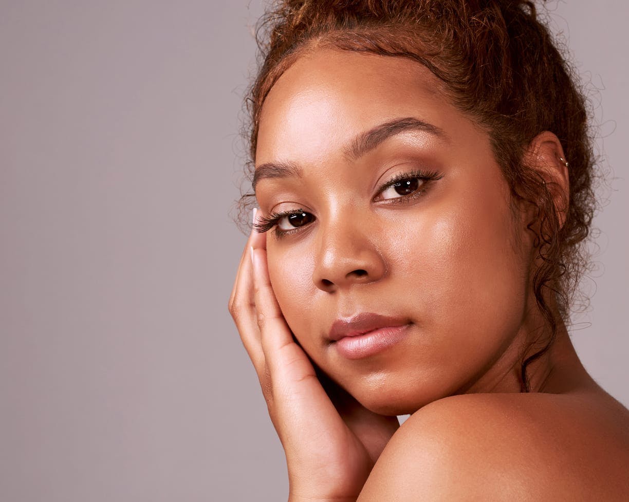 Woman with clear skin looking towards the camera with her hand on her face