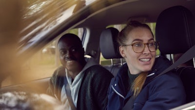 A man and woman sitting in a car, smiling and looking in the same direction.