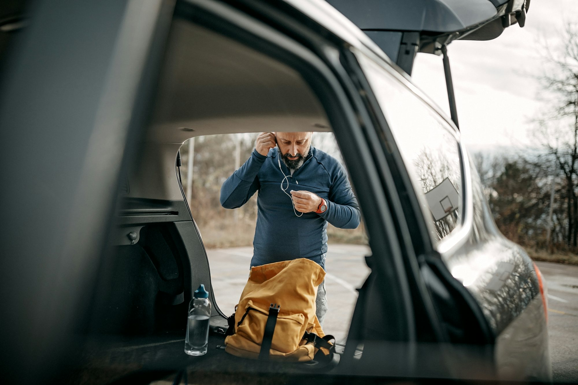 En man syns genom en bildörr, han står bakom bilen genom med öppen baklucka och sätter på sig hörlurar.