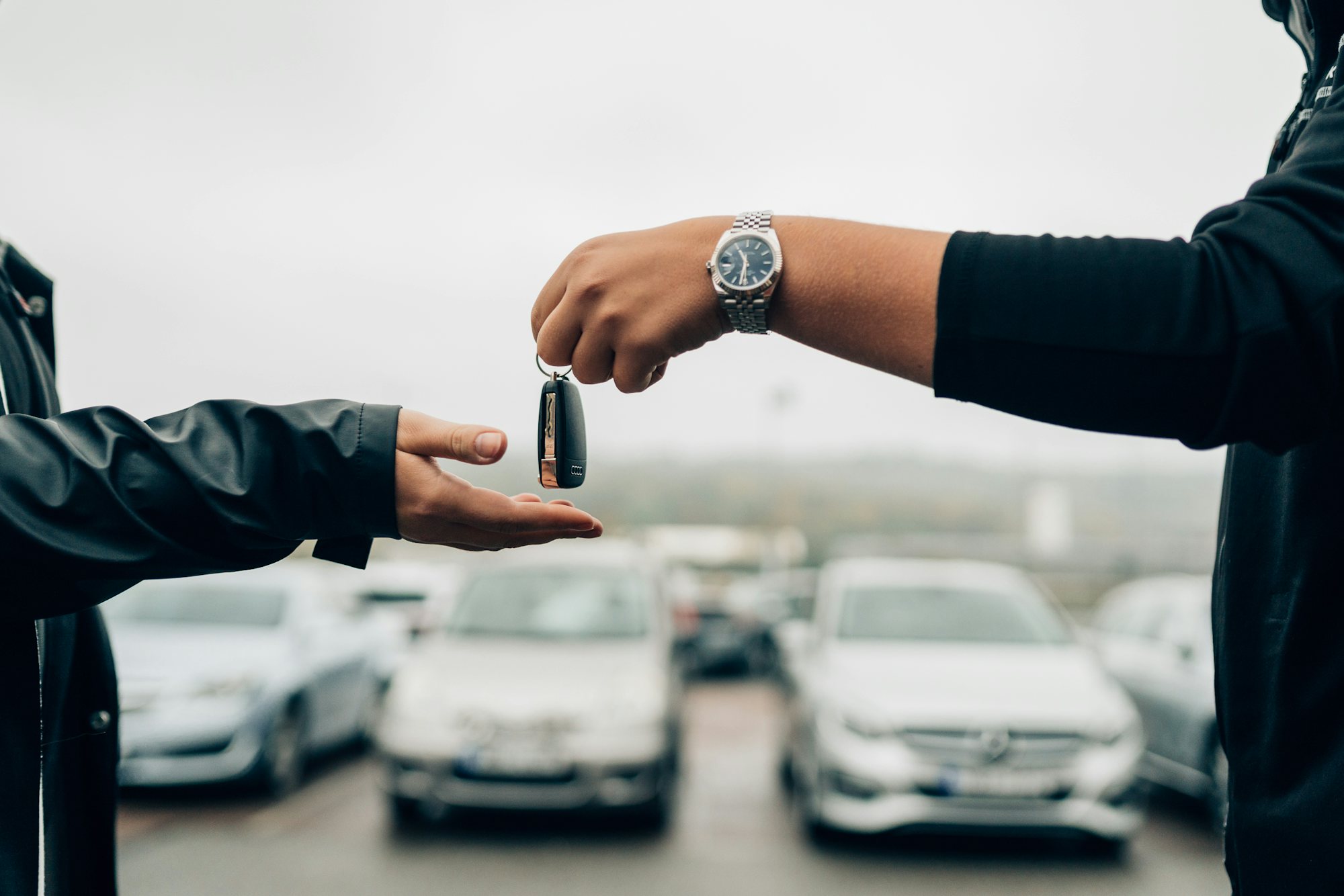 En person överlämnar en bilnyckel till en annan person på en bilparkering.