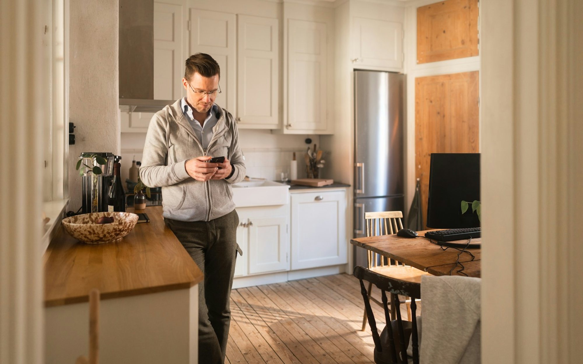 En man står i ett kök och tittar på sin mobiltelefon