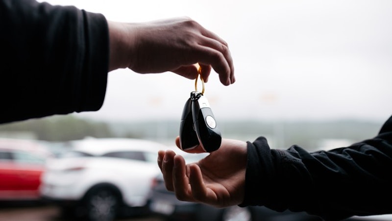 En person lämnar över en bilnyckel till en annan person på en parkering