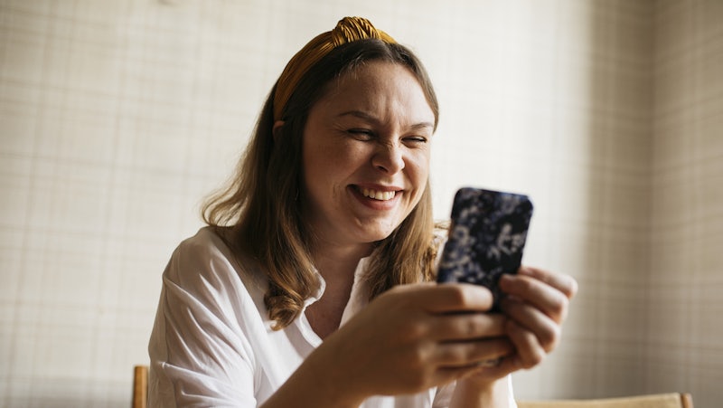 En kvinna sitter i en stol och tittar på sin mobiltelefon.