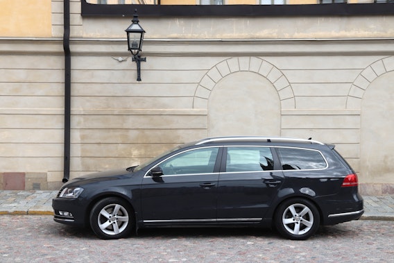 En svart Volkswagen Passat står parkerad framför en byggnad.