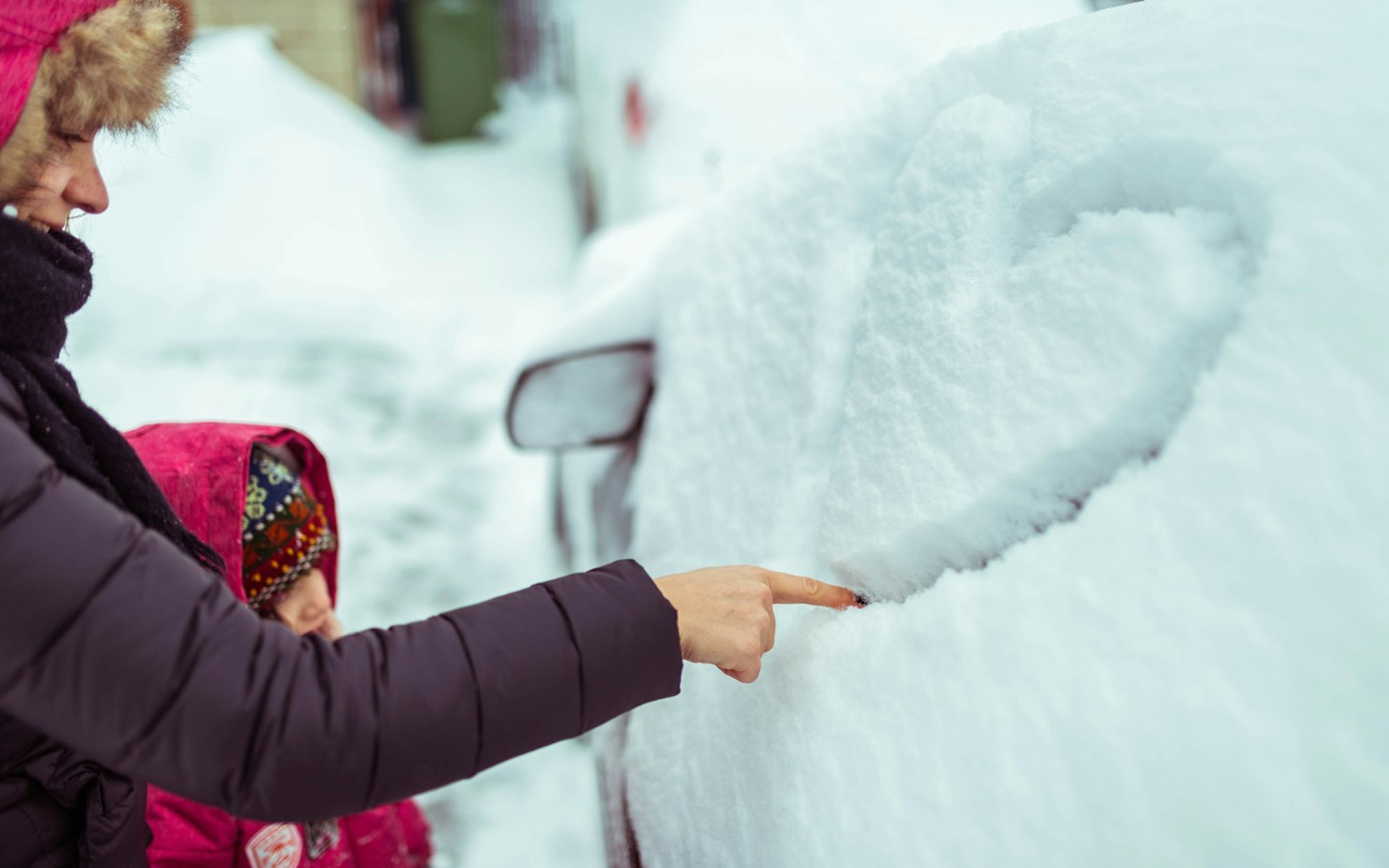 Vuxen och barn ritar ett hjärta i snön som täcker bilens sidoruta en vinterdag.