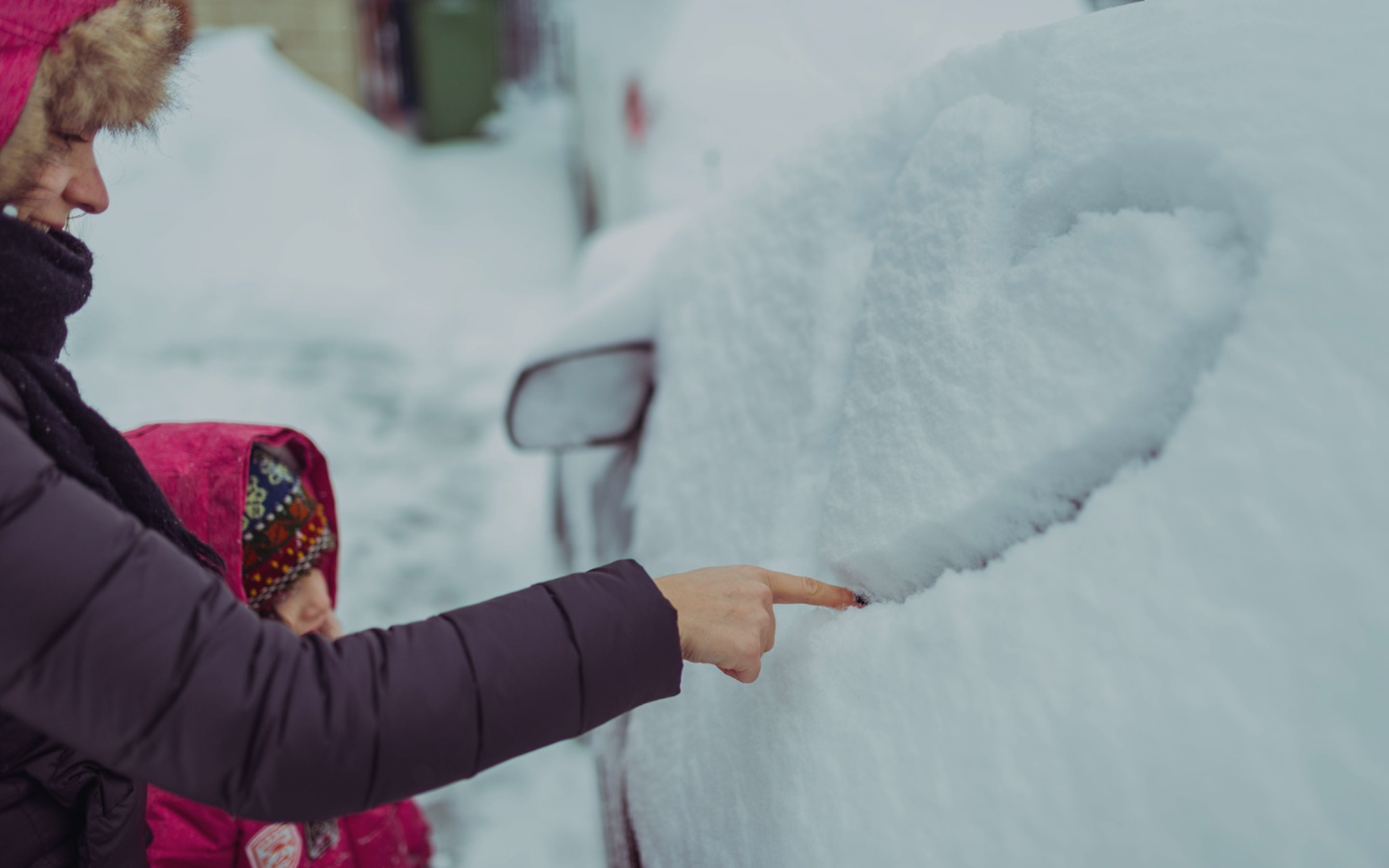 Vuxen och barn ritar ett hjärta i snön som täcker bilens sidoruta en vinterdag.