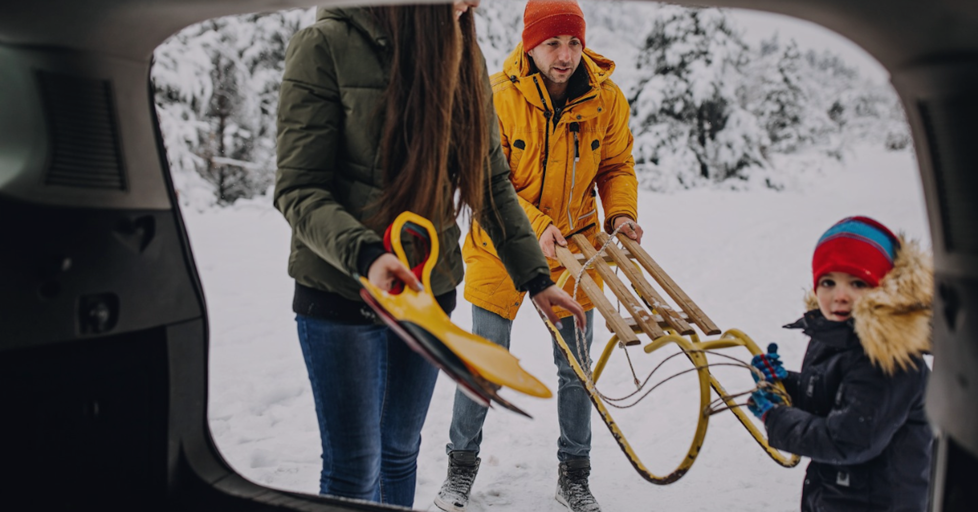 Familj lastar pulkor ur bilens bagageutrymme i ett snötäckt vinterlandskap.