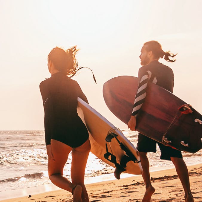 two people walking with surf boards on the beach