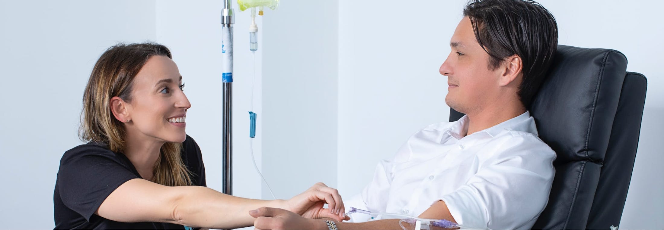 Female Nurse Smiling, Administering a Vitamin IV Drip to a Young Man Sitting in a Recliner Chair at Prosper IV