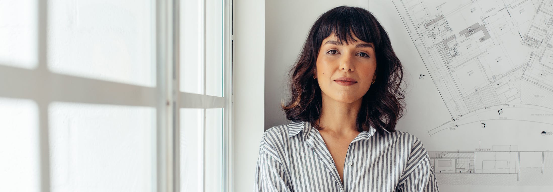 Woman with short hair standing against a building floor plan