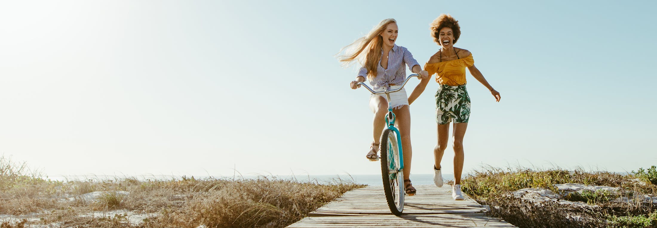 Two women running and biking down a beach board walk