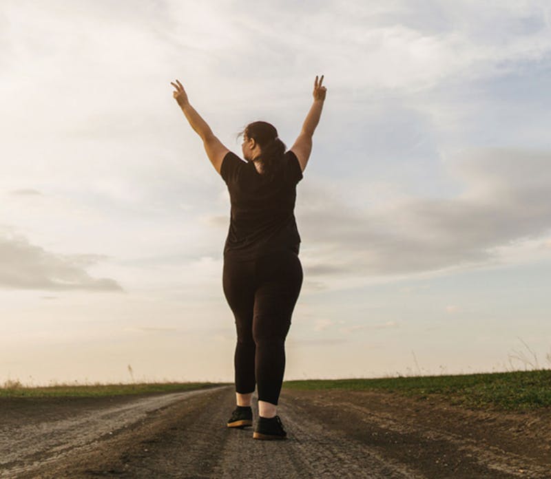 Woman with arms in the air walking down trail