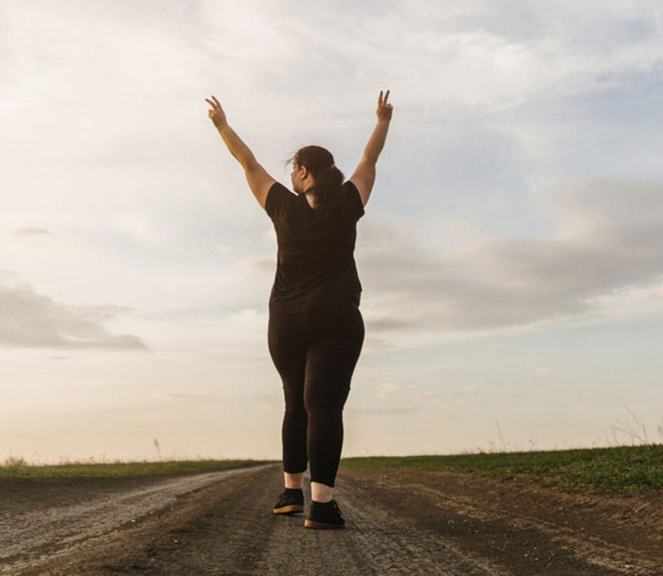 Woman with arms in the air walking down trail