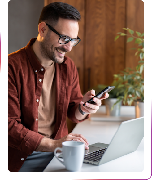 young guy using phone and laptop smiling