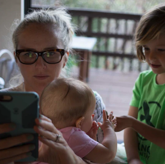 Kvinna kollar på mobil medans hon tar hand om två små barn