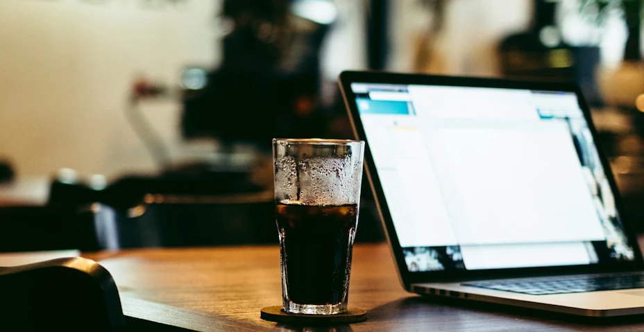 Glass med caffe står brevid laptop på skfivbord