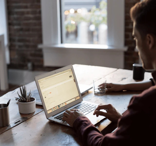 Man viewed from behind in front of laptop computer on desk in open office