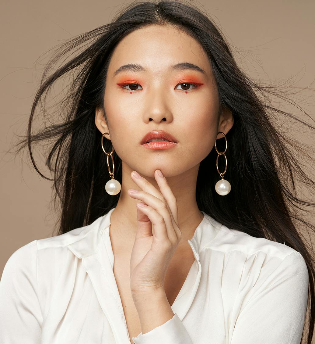 woman with orange eyeshadow on and pearl earrings