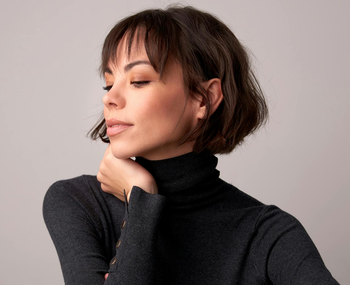 woman with short brown hair and bangs and black turtleneck on