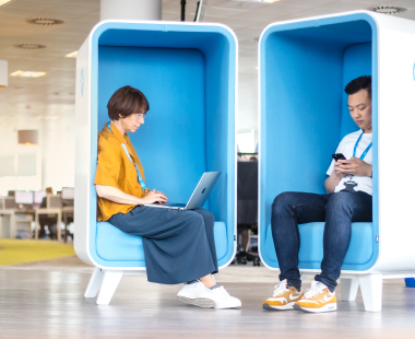 Two people sat on chairs. Woman with laptop on her lap and man looking at the phone in his hands.