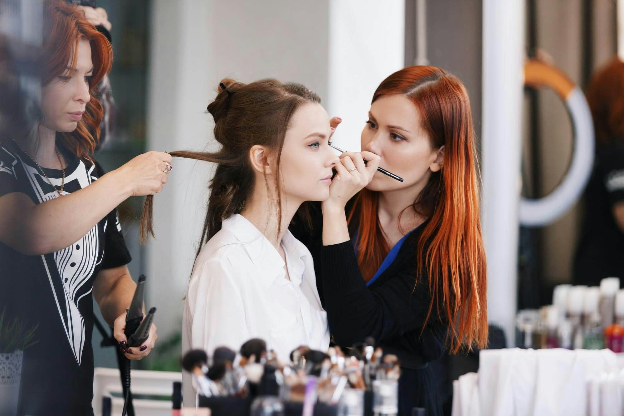 Two women applying makeup and styling a client's hair
