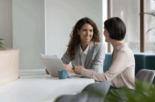 Two people smiling and chatting around a laptop