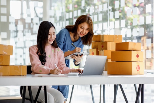 Two women looking at a computer surrounded by packed up boxes,