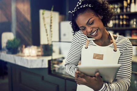 A woman wearing an apron, making notes on a tablet while talking on the phone