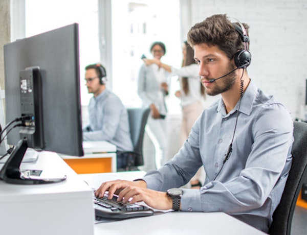 A man wearing a phone headset while sitting at a desk with a computer