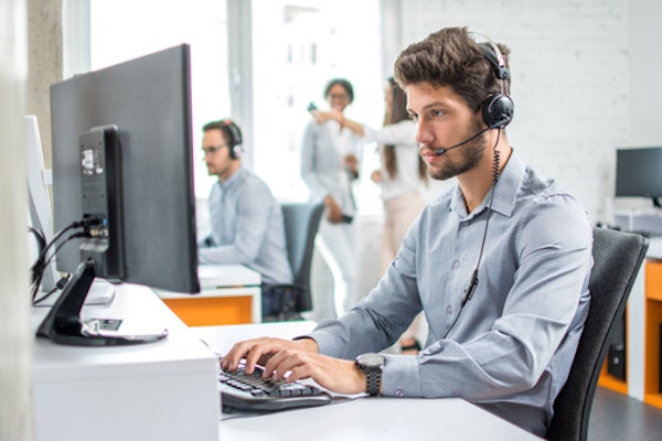 A man wearing a phone headset while sitting at a desk with a computer