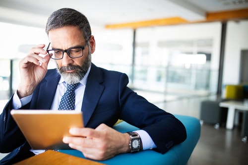 A man in a suit reading from a tablet while in an office setting