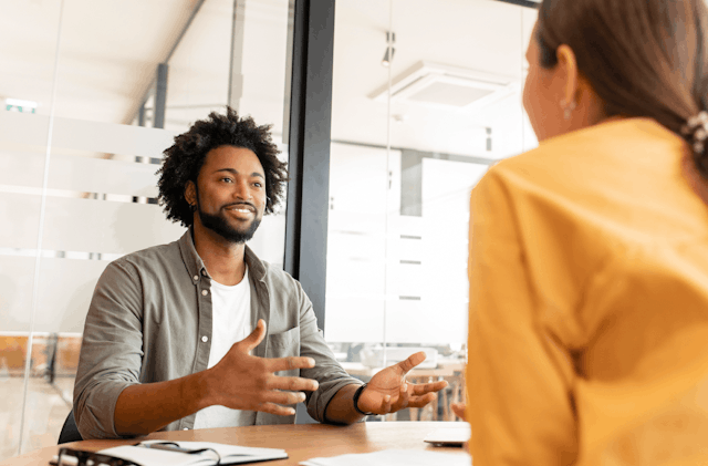 Two workers sat across a desk from each other having a conversation.