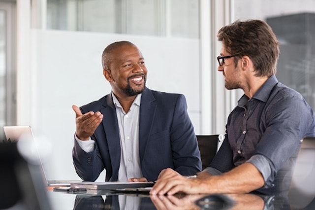 Two businessmen talking while sat at a desk
