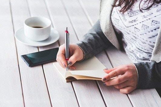 someone sat at a desk with a coffee making notes