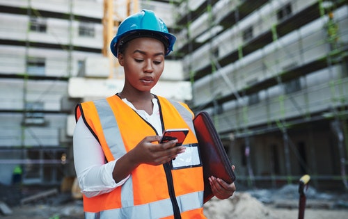 a young construction worker wearing PPE checking their phone