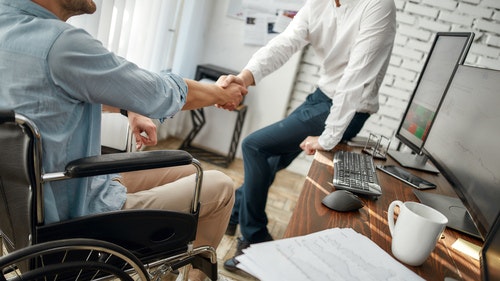 A man in a wheelchair shaking hands with someone sat on their desk