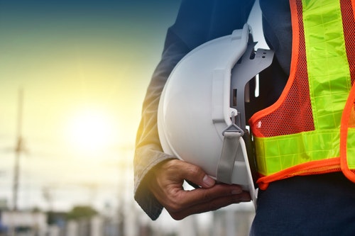 A construction worker holding a hard hat wearing a hi vis jacket