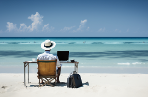 A man sat at his desk on the beach, looking out at the sea.