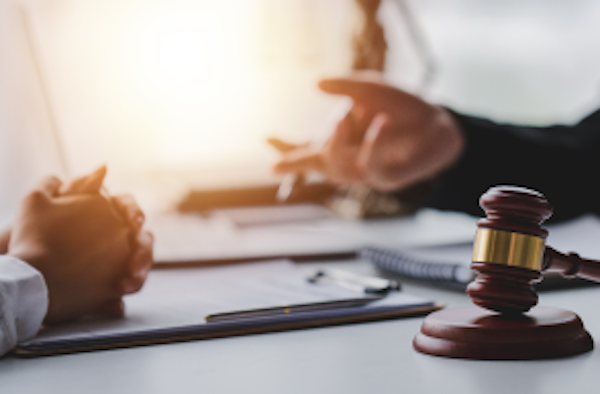 two people sit across a table full of documents, a gavel is in the foreground.