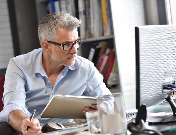 A man is looking at a computer screen and holding a tablet.