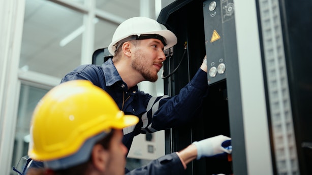 Two men in helmets looking at a piece of machinery