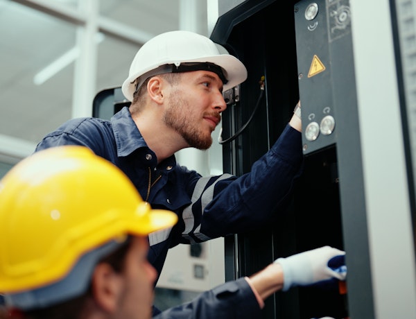 Two men in helmets looking at a piece of machinery