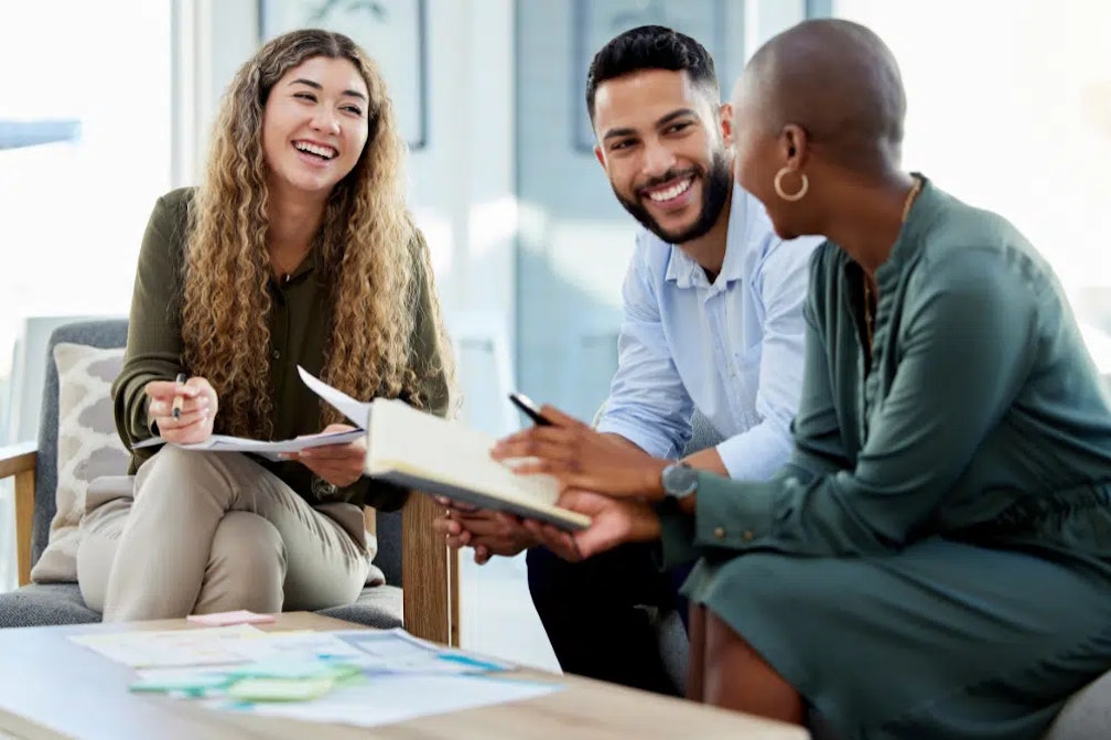 three people sitting around a coffee table smiling
