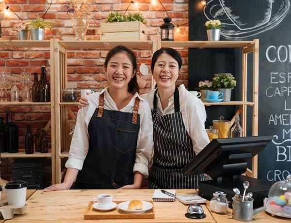Two smiling workers stand behind a till.