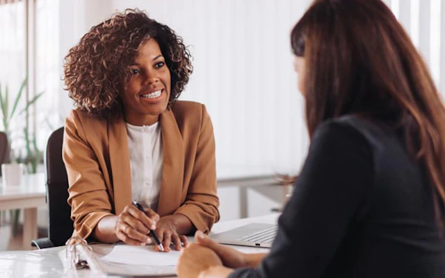 Two women discuss paperwork at a desk