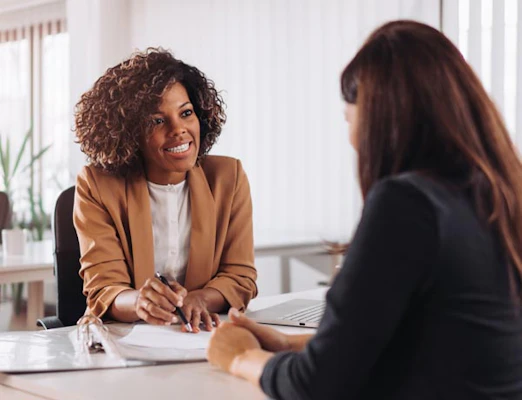 Two women discuss paperwork at a desk