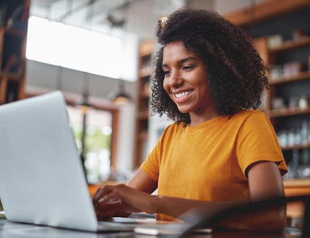 A smiling woman works on a laptop.