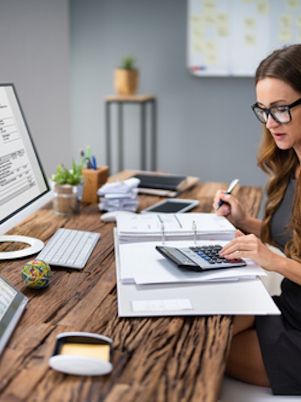 a woman at a desk with paperwork and a calculator and a computer